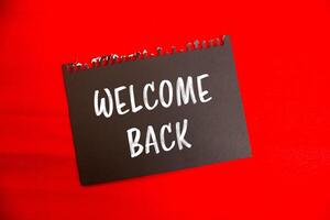 Welcome back message written on black notebook page paper with red background. Conceptual welcome back symbol. Copy space. photo