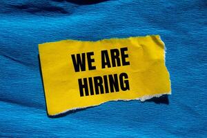 We are hiring message written on ripped torn yellow paper piece with blue background. Conceptual we are hiring symbol. Copy space. photo