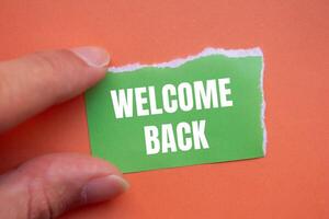 Welcome back message written on ripped green torn paper piece with orange background. Conceptual welcome back symbol. Copy space. photo