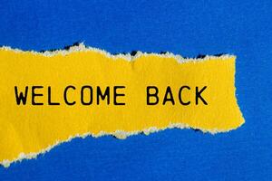 Welcome back message written on ripped torn yellow paper piece with blue background. Conceptual welcome back symbol. Copy space. photo