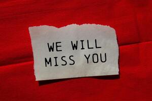 We will miss you message written on ripped torn paper piece on red background. Conceptual we will miss you symbol. Copy space. photo