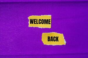 Welcome back message written on ripped torn yellow paper pieces with purple background. Conceptual welcome back symbol. Copy space. photo