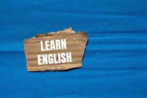 Learn english message written on ripped torn cardboard paper piece with blue background. Conceptual learn english symbol. Copy space. photo