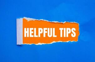 Helpful tips message written on ripped torn blue paper with orange background. Conceptual helpful tips symbol. Copy space. photo