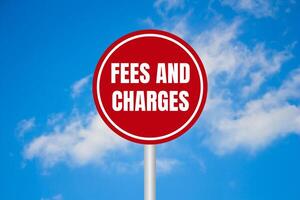 Fees and charges message written on red round sign on blue sky background. Conceptual fees and charges symbol. Copy space. photo