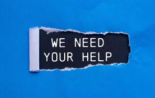We need your help message written on ripped torn blue paper with black background. Conceptual we need your help symbol. Copy space. photo