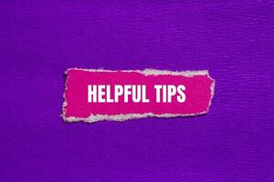 Helpful tips message written on ripped torn pink paper piece with purple background. Conceptual helpful tips symbol. Copy space. photo