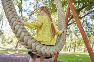 Young girl with braided hair enjoying a rope swing in a sunny park surrounded by lush greenery. photo