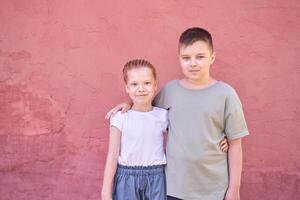 Siblings smiling together in front of a red wall outdoors on a sunny day. photo