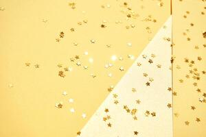 Golden star confetti scattered on yellow background with textured paper and sparkling highlights. photo