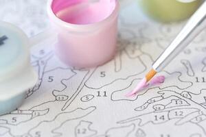 Detailed close-up of painting by numbers with paintbrush and pink paint on canvas with numbered sections. photo