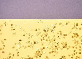 Sparkling gold star confetti scattered on yellow paper background with minimal design elements. photo