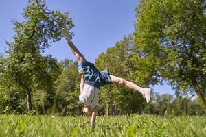 Joyful child performing cartwheel in sunny park surrounded by lush greenery and bright blue sky. photo