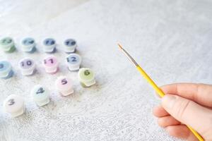 Hand holding brush over paint by numbers canvas with colorful paint pots for creative diy art and relaxation. photo