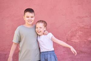 Happy siblings hugging in front of pink wall on a sunny day. photo