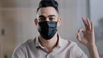 Happy hispanic male employee arabian man entrepreneur wear medical mask prevent coronavirus epidemic looking at camera showing okay sign everything fine success gesture body language good mood symbol photo