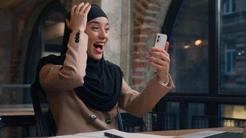 contento emocionado alegre árabe musulmán negocio mujer preguntarse asombro hembra islámico niña hijab usuario estudiante mujer de negocios móvil teléfono bueno Noticias lograr victoria en línea apuesta conmoción ganar teléfono inteligente oficina foto