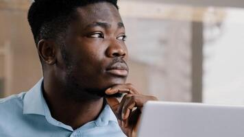Thoughtful african american businessman writer dreamer genius man biracial guy holds hand on chin creates business plan come up with idea for startup uses computer typing text creates internet project photo
