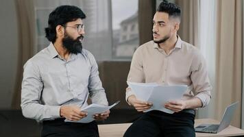 Multiracial diverse co-workers businessmen partners sit on desk hispanic expert consult arabian man colleague hold stack of paper documents discuss financial data insurance contracts teamwork concept photo