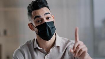 Arabian businessman employee wear medical mask sit at office desk shakes wave index finger warn illnesses infection showing no gesture disagreement sick isolated man avoid offer with negative gesture photo