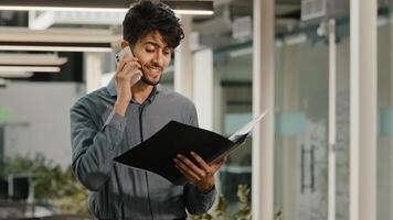 Busy arab man businessman worker in office workspace talking mobile phone answer call consulting clients discussing financial issues holds folder documents statistical data negotiating project profit photo