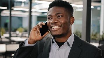 African business analyst manager smiling man speaking on cell phone customer consulting communicating emotionally indoor telling story making online order arrange meeting colleague in empty office photo