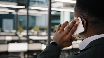 African American man confident businessman team leader manager call business partner communicate with friend talk on smartphone discuss distant negotiation with colleague hold mobile phone back view photo