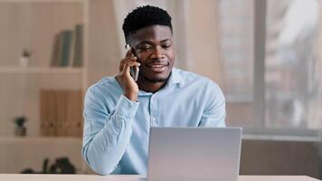 African american man businessman freelancer worker talk chatter on mobile cellphone with client make business call discussion listen news explain information looks at laptop screen use gadget service photo