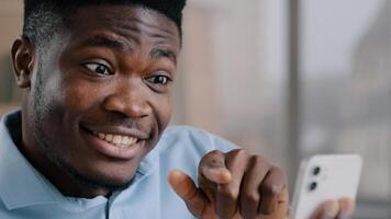 Smiling happy african man businessman adviser american brunet guy expert hold mobile phone look at display smartphone gadget greet friend by call communicate in virtual chat remote consultation photo