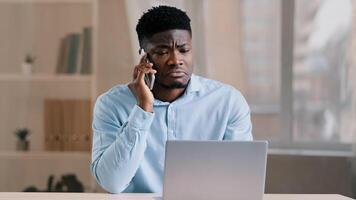 African american man businessman freelancer worker talk chatter on mobile cellphone with client make business call discussion listen news explain information looks at laptop screen use gadget service photo