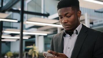 Thoughtful African man professional broker using mobile apps for online sales chatting with friend making order surfing internet focused analyst reading information typing message in social network photo