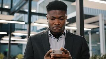 Serious young man african american office worker searching smartphone internet choosing making order chatting online with friends scrolling mobile phone thoughtful male user click at browser account photo