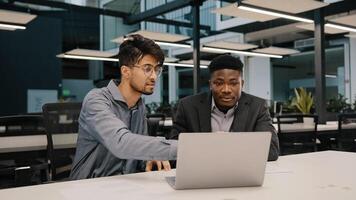 Two multicultural professional male co-workers men colleagues sit at office use laptop discuss internet project hold negotiation choosing business profitable contract cooperation teamwork partnership photo