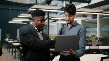 Two male business partners men Arabian man holding laptop showing presentation African businessman looking at computer screen colleagues working online discuss startup pointing display making choice photo
