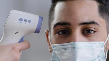 Close-up view infrared scanner on male customer's forehead arabian man in protective medical mask scanning body temperature patient measuring fever by digital electronic thermometer covid-19 checking photo