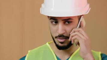 Close up shot of young hispanic man engineer construction foreman builder in special safety helmet talking cell phone with building worker discussing blueprint background neon emergency illumination photo