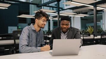 Two multicultural professional male co-workers men colleagues sit at office use laptop discuss internet project hold negotiation choosing business profitable contract cooperation teamwork partnership photo