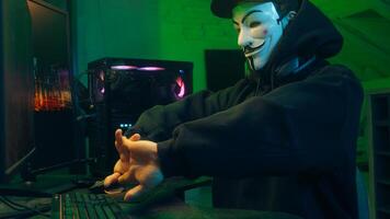 Lviv, Ukraine - June 03, 2024. Masked man anonymous stretching fingers programmer hacking typing computer malware networks web danger scam database spy system virus theft server break cryptocurrency photo