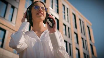 despreocupado contento mujer escuchando audio música en auriculares utilizando móvil mp3 solicitud en teléfono bailando canto al aire libre en céntrico sonriente niña mujer de negocios disfrutando favorito canción en ciudad canta danza foto