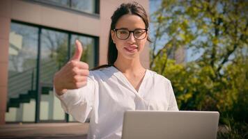 Smiling Caucasian woman girl female businesswoman freelancer student using laptop in city outdoors showing thumbs up gesture approval recommending service approving advertising computer application photo