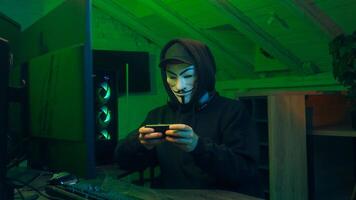 Lviv, Ukraine - June 03, 2024. Man in mask using mobile phone smartphone anonymous looking at camera technology program secure stealing danger banking cyber crime virtual hack binary password computer photo