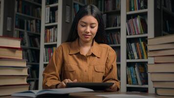 Asian woman female girl student in university library preparing exam studying using digital tablet reading ebook checking task list timetable class use application study education modern technology photo