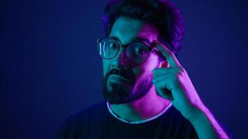Indian man developer coding worker computer smart clever hacker in glasses neon ultraviolet studio background thinking hard brain power mental strength think about it ponder problem solving IQ gesture photo