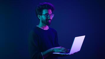 Arabian Indian man guy male programmer coder employer freelancer working using internet computer developer businessman business guy gamer hold laptop computer work in violet neon background network photo