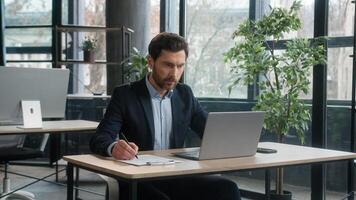 Focused adult businessman work on project in office using laptop writing notes caucasian man business leader professional employee analyze information on internet write data planning with computer app photo