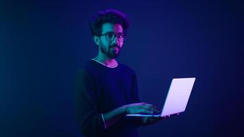 Arabian Indian man guy male programmer coder employer freelancer working using internet computer developer businessman business guy gamer hold laptop computer work in violet neon background network photo