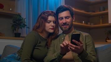contento familia caucásico casado Pareja marido esposa hombre mujer compras en en línea Tienda en acogedor sofá a hogar noche utilizando móvil solicitud en teléfono ordenando entrega juntos hablando Internet comprando foto