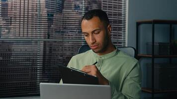 African american man manager looking at laptop screen writing financial report analyzing data from internet young ethnic businessman write notes doing paperwork in office workplace making presentation photo