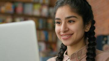 Close-up smiling young indian woman looking at laptop screen indoors checking email browsing social network hispanic girl student studying online remote chatting on internet typing message on computer photo