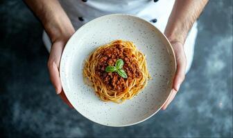 Chef holding plate of Bolognese pasta, close-up, top view, dark background with copy space photo